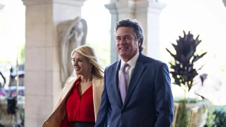 John Goodman and a woman walking together through an elegant, columned building entrance, both dressed in formal attire.