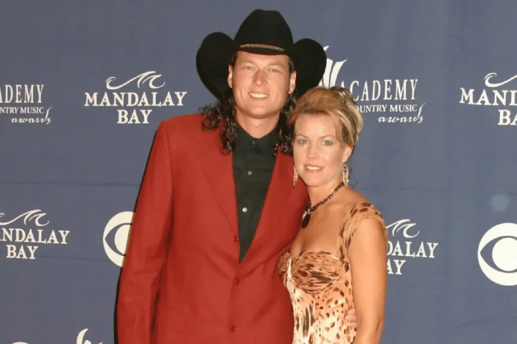 Blake Shelton in a red blazer and black cowboy hat posing on the red carpet with Kaynette Williams in a patterned dress at Mandalay Bay.