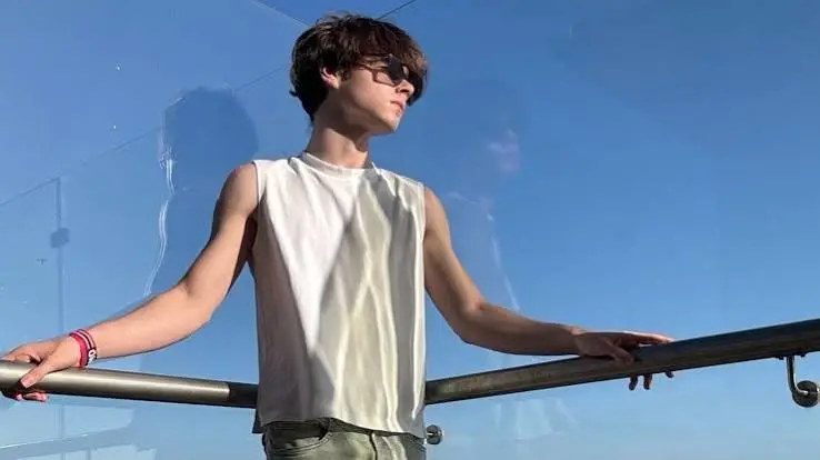Valentino Martin wearing sunglasses and a sleeveless white shirt while standing beside a railing under a clear blue sky.
