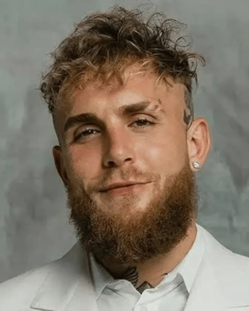 Close-up portrait of Jake Paul wearing a white collared shirt with his head tattooed and beard styled