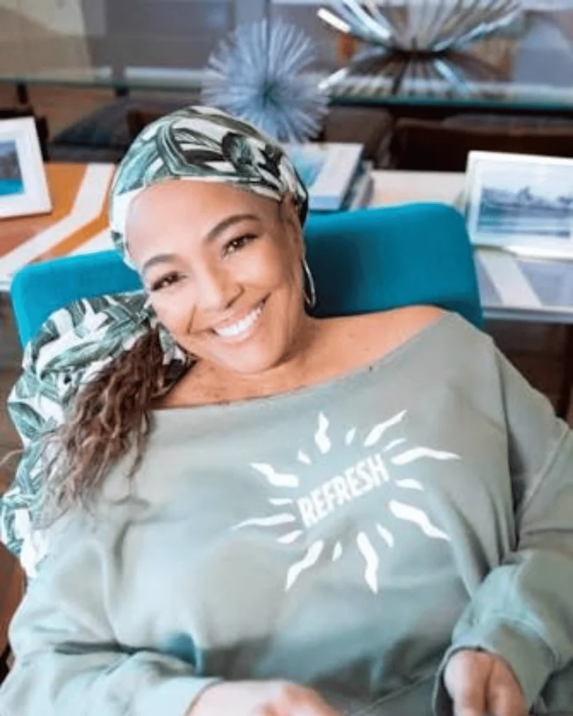 Kim Fields smiling warmly in a light green Refresh sweatshirt and matching leaf-patterned headwrap.