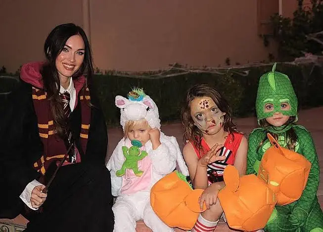 Megan Fox posing with three children in Halloween costumes.