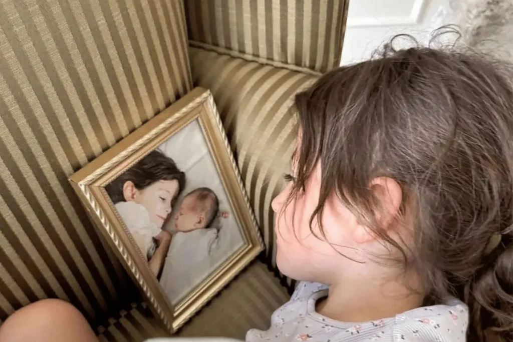 Melissa Mae Carlton's daughter Molly looking at a framed photo with her late sister Abigail