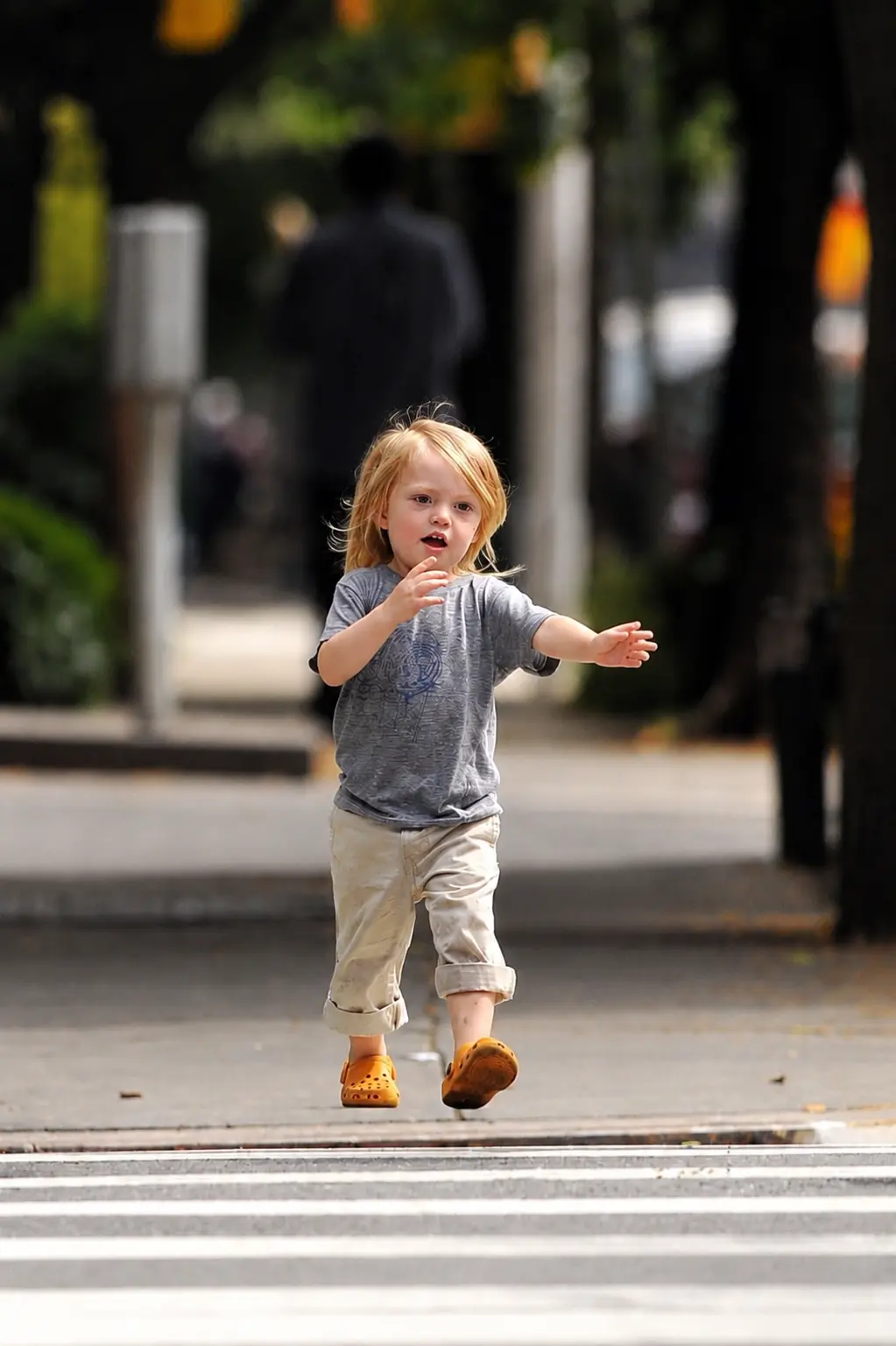 River Russell walks across a city street wearing a gray T-shirt, rolled-up beige pants, and orange shoes.