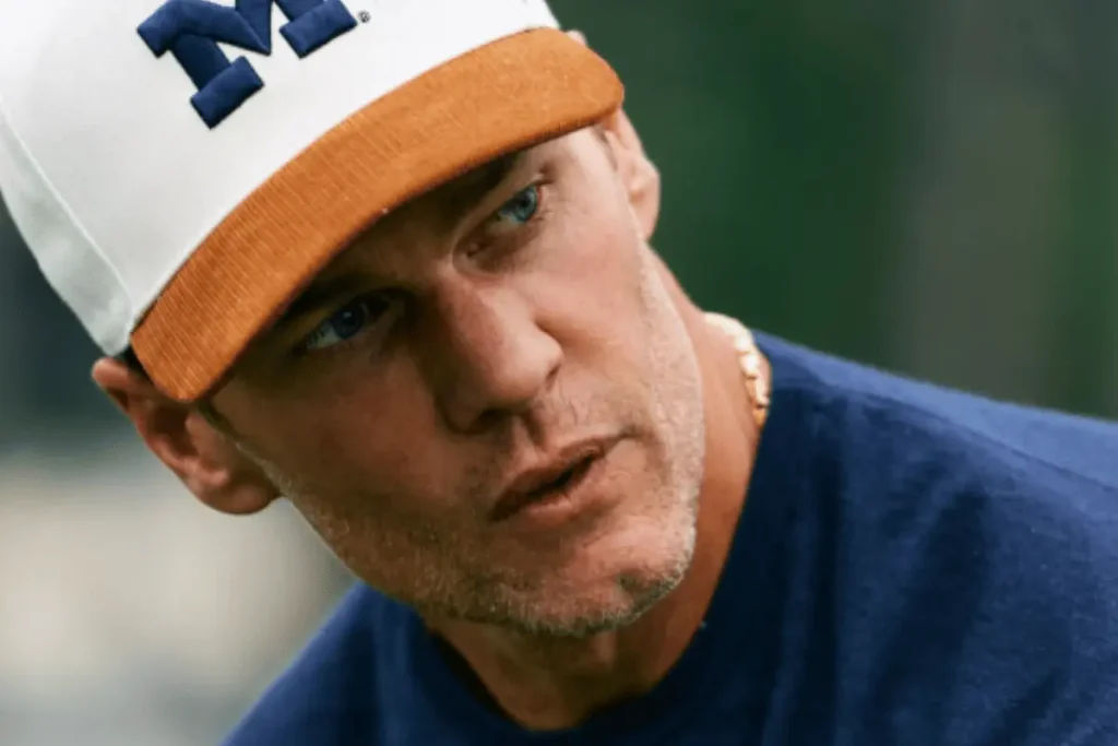 Tom Brady wearing a white and orange cap in a close-up portrait