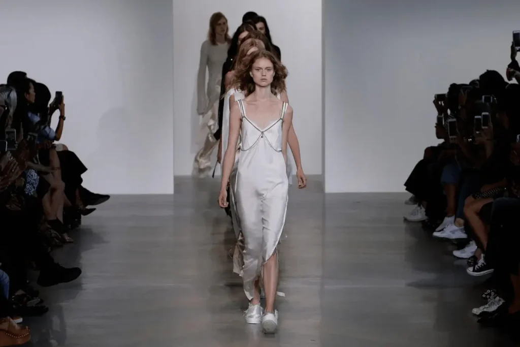 Models walk a Calvin Klein runway in minimalist dresses and neutral colors.
