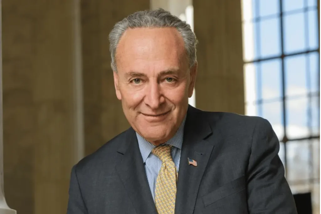 Chuck Schumer wearing a dark suit and yellow patterned tie in his official Senate portrait.
